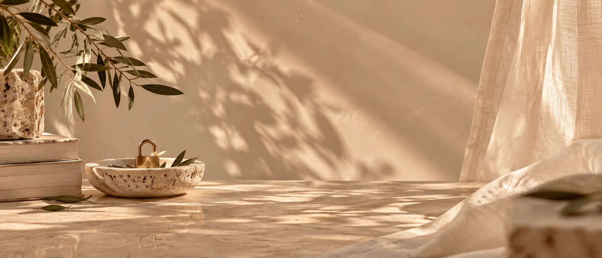 A stone dish holding a brass padlock, beside a stack of books and a linen curtain.